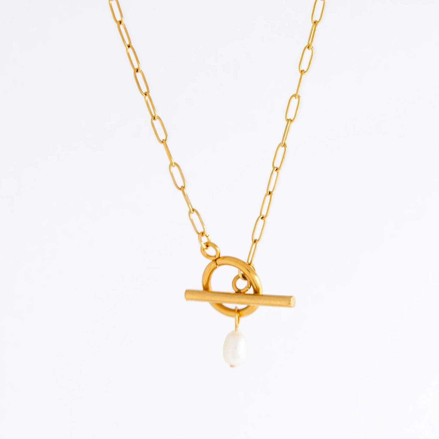 Gold paperclip necklace with toggle clasp and a pearl pendant on a light gray background