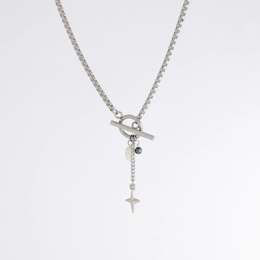 Silver box chain necklace with a toggle clasp and a few charms including freshwater pearl, black glass bead and a dangling star chain on a light gray background