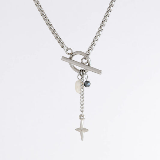 Silver box chain necklace with a toggle clasp and a few charms including freshwater pearl, black glass bead and a dangling star chain on a light gray background