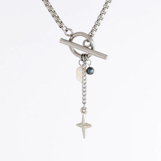 Silver box chain necklace with a toggle clasp and a few charms including freshwater pearl, black glass bead and a dangling star chain on a light gray background