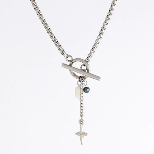 Silver box chain necklace with a toggle clasp and a few charms including freshwater pearl, black glass bead and a dangling star chain on a light gray background