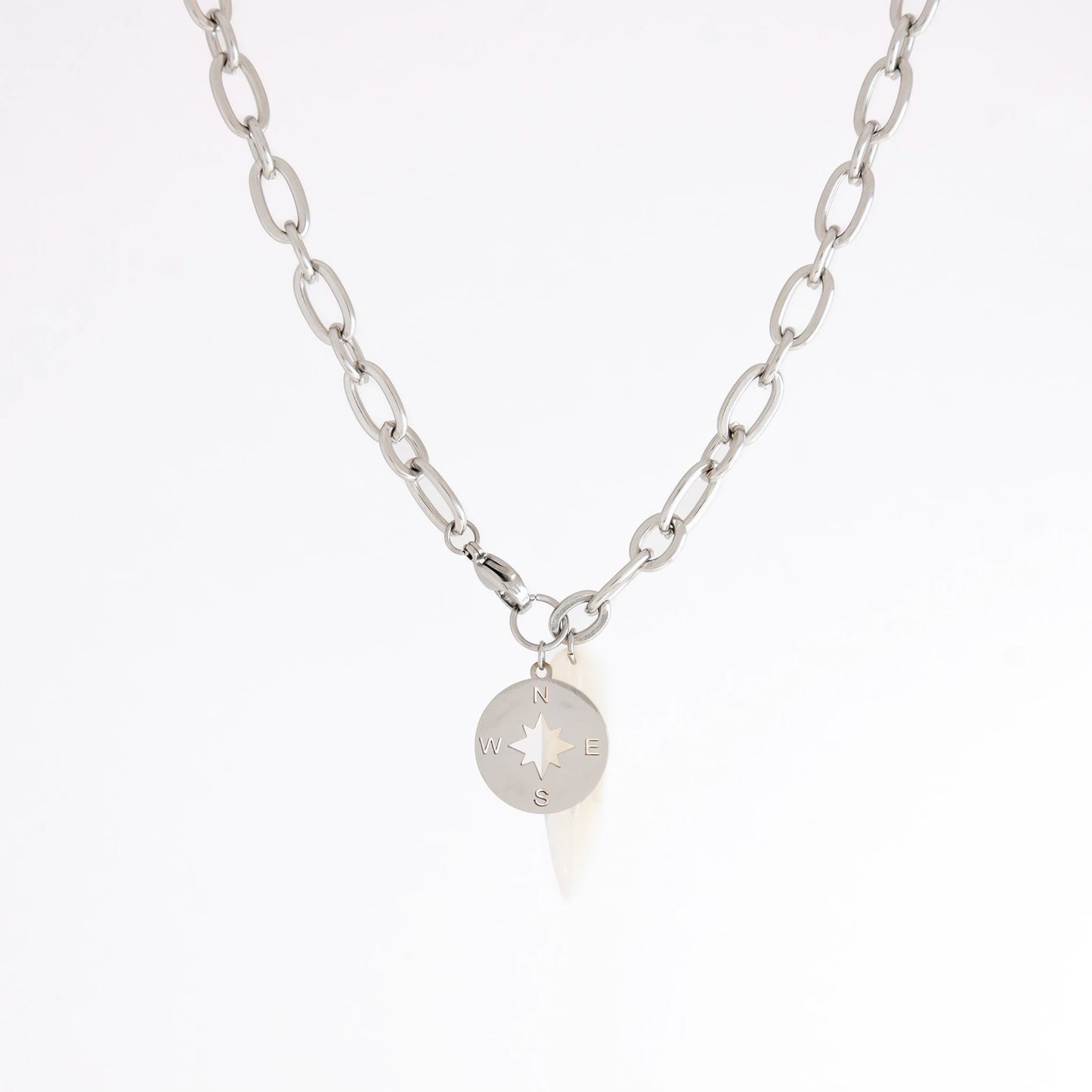A silver chain necklace featuring a small circular compass pendant with cardinal directions, displayed against a clean white background.