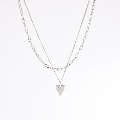 A layered silver necklace set featuring a paperclip chain and a chain with a small heart-shaped pendant, displayed against a clean white background.