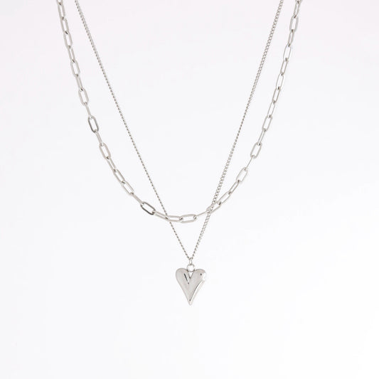 A layered silver necklace set featuring a paperclip chain and a chain with a small heart-shaped pendant, displayed against a clean white background.