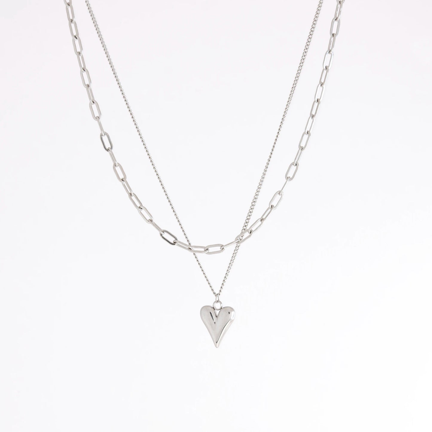 A layered silver necklace set featuring a paperclip chain and a chain with a small heart-shaped pendant, displayed against a clean white background.
