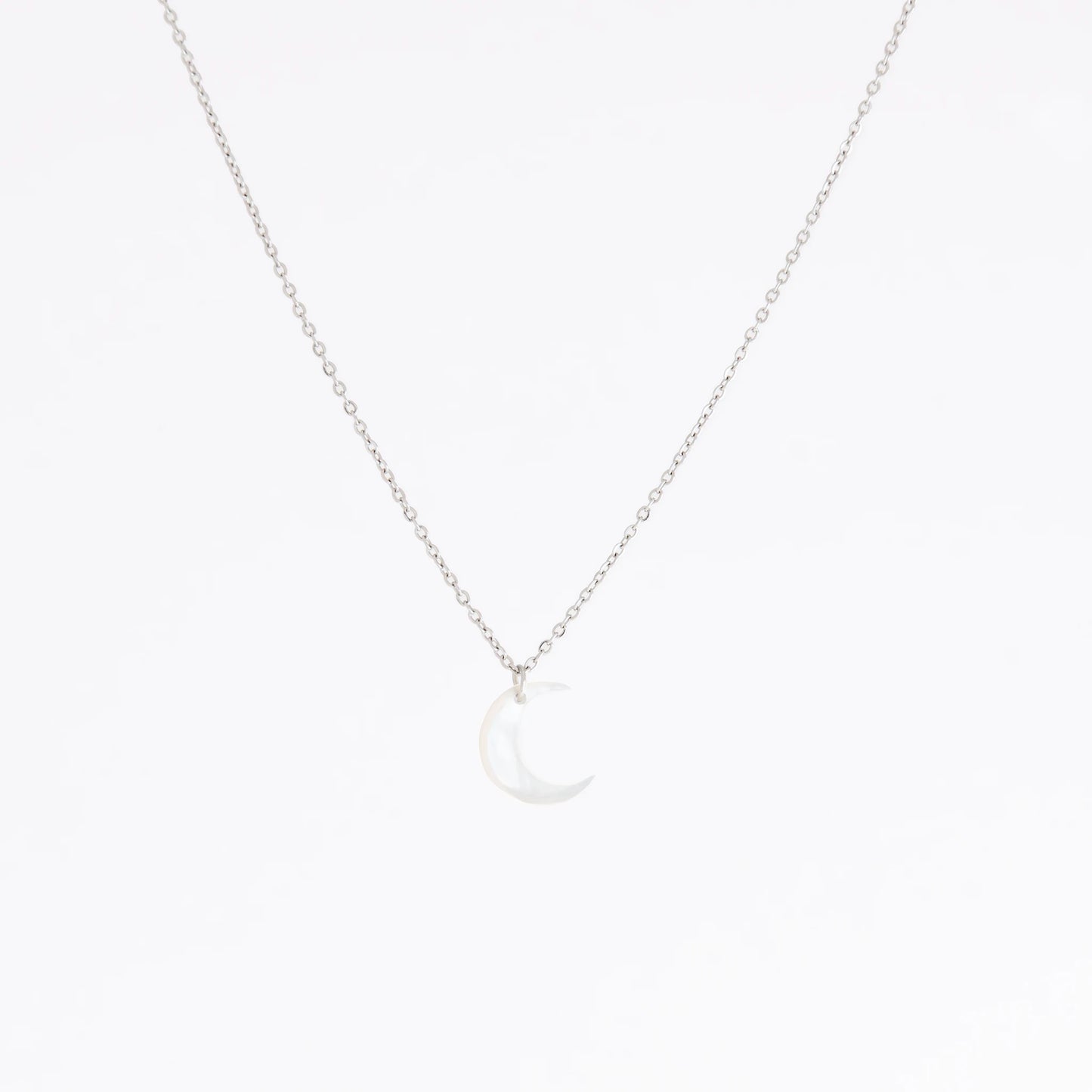 A delicate silver chain necklace featuring a small crescent moon pendant made of milky white mother-of-pearl, set against a seamless white background.