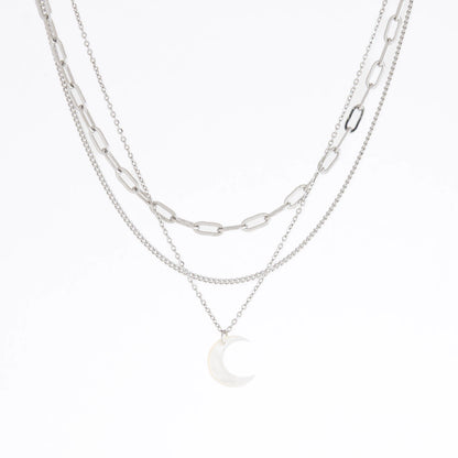 A layered silver necklace featuring a paperclip chain, a fine chain, and a small crescent moon pendant, displayed on a clean white background.