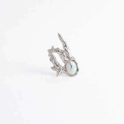 A silver ring featuring a textured, organic branch-like setting with a round iridescent opal gemstone, photographed on a seamless white background.