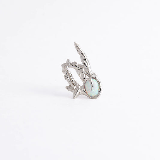 A silver ring featuring a textured, organic branch-like setting with a round iridescent opal gemstone, photographed on a seamless white background.