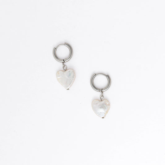 A pair of silver huggie hoop earrings with dangling heart charms made of freshwater heart pearl, shown on a clean white background.