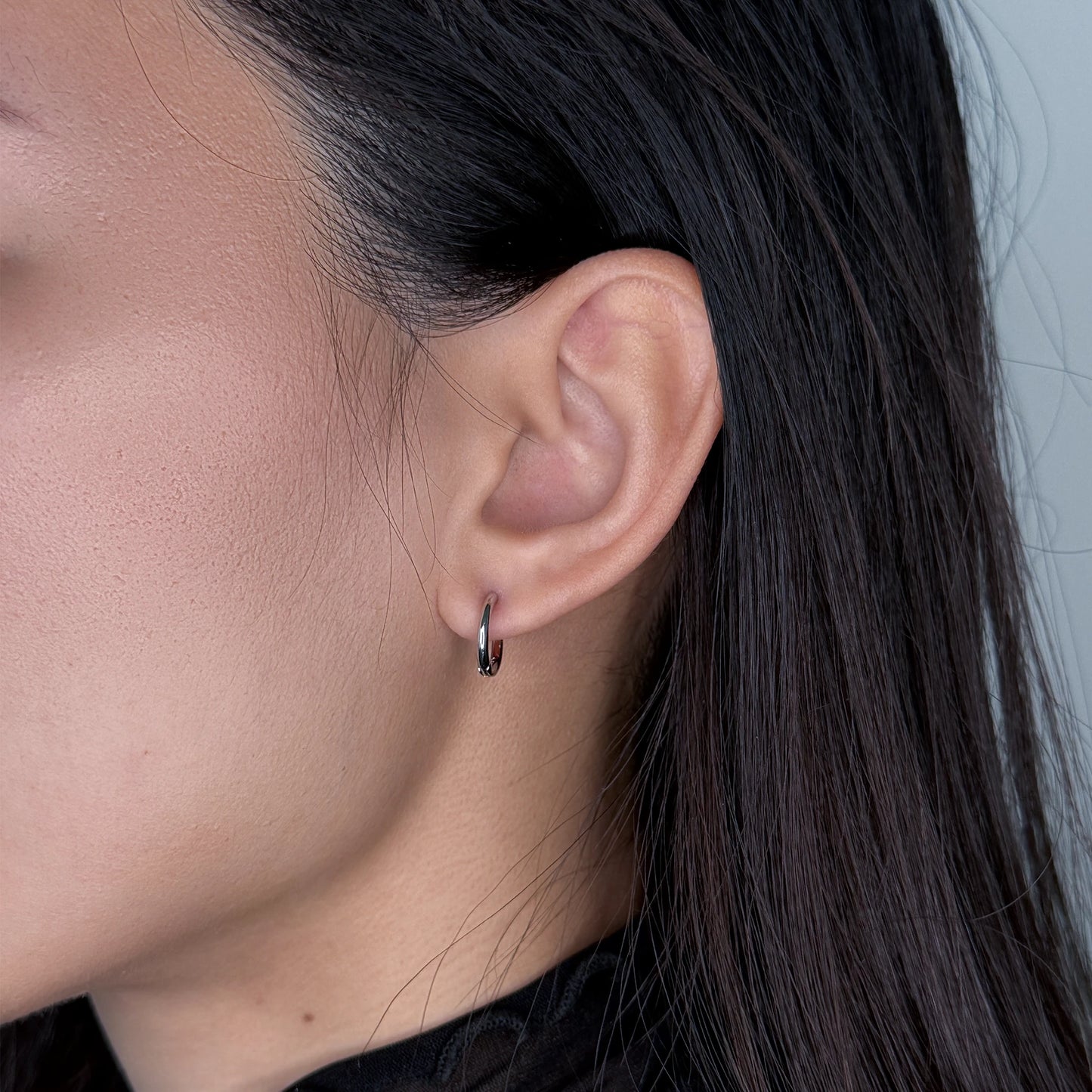 Silver huggies hoop earrings worn by model on a gray background