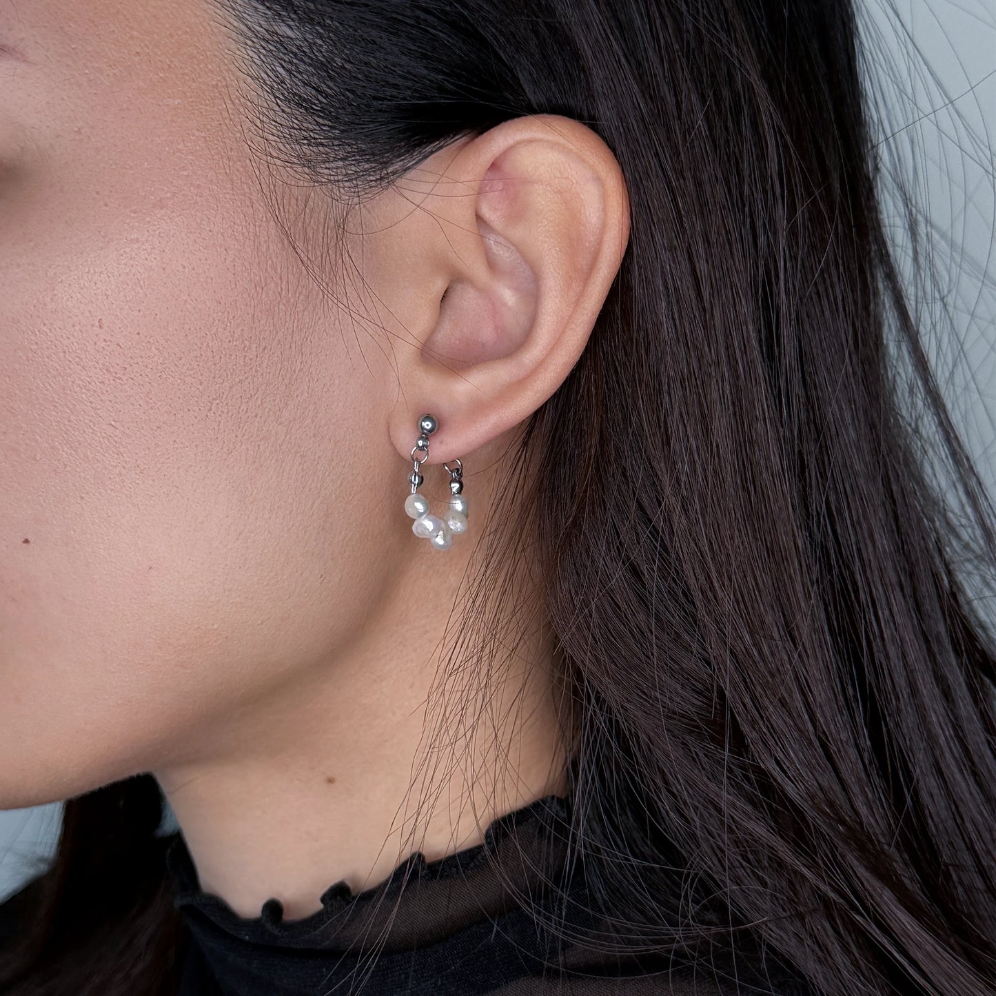 Silver pearl hoop earrings worn by model on a gray background