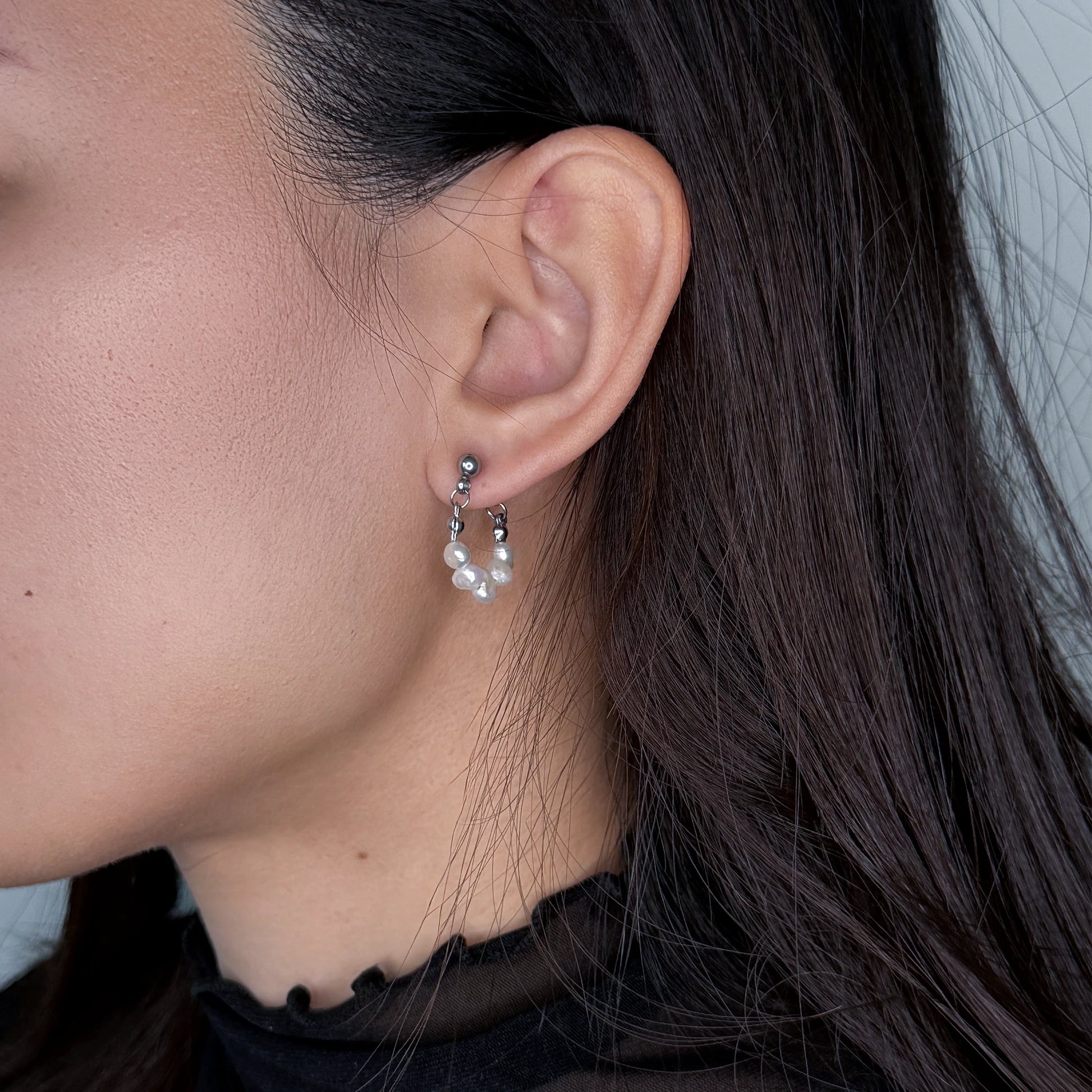 Silver pearl hoop earrings worn by model on a gray background