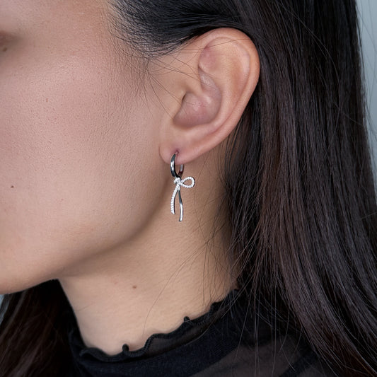 Silver ribbon hoop earrings worn by model on a gray background