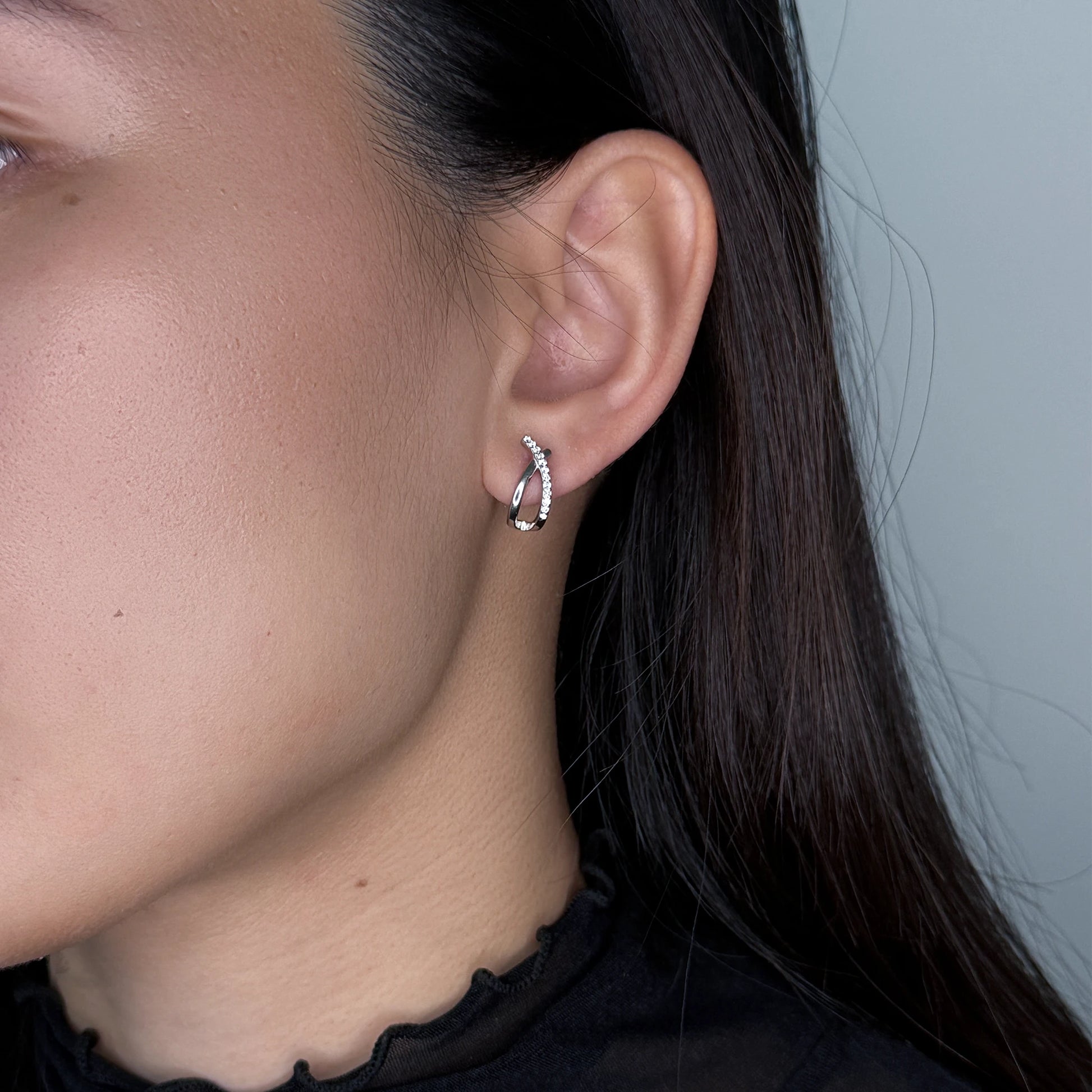 Silver crossed stud earrings worn by model on a gray background