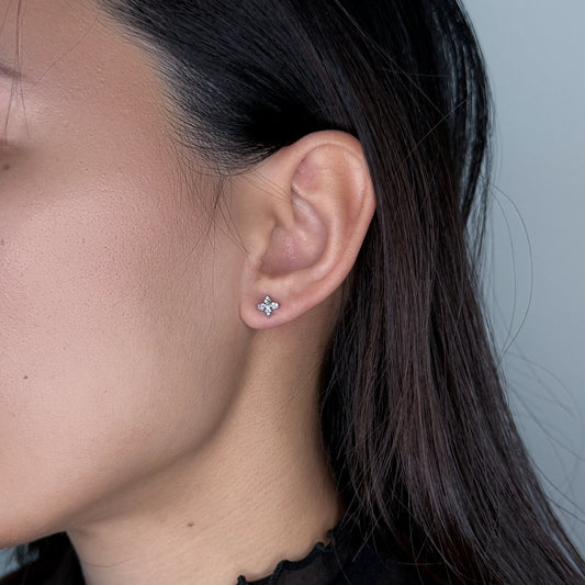 Silver clover star studs worn by model on a gray background