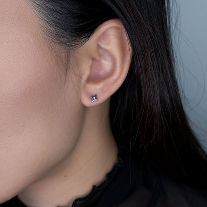 Silver clover stud earrings worn by model on a gray background