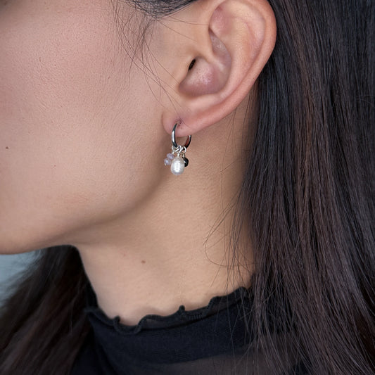 Silver huggies hoop earrings with pearl and glass charms worn by model on a gray background