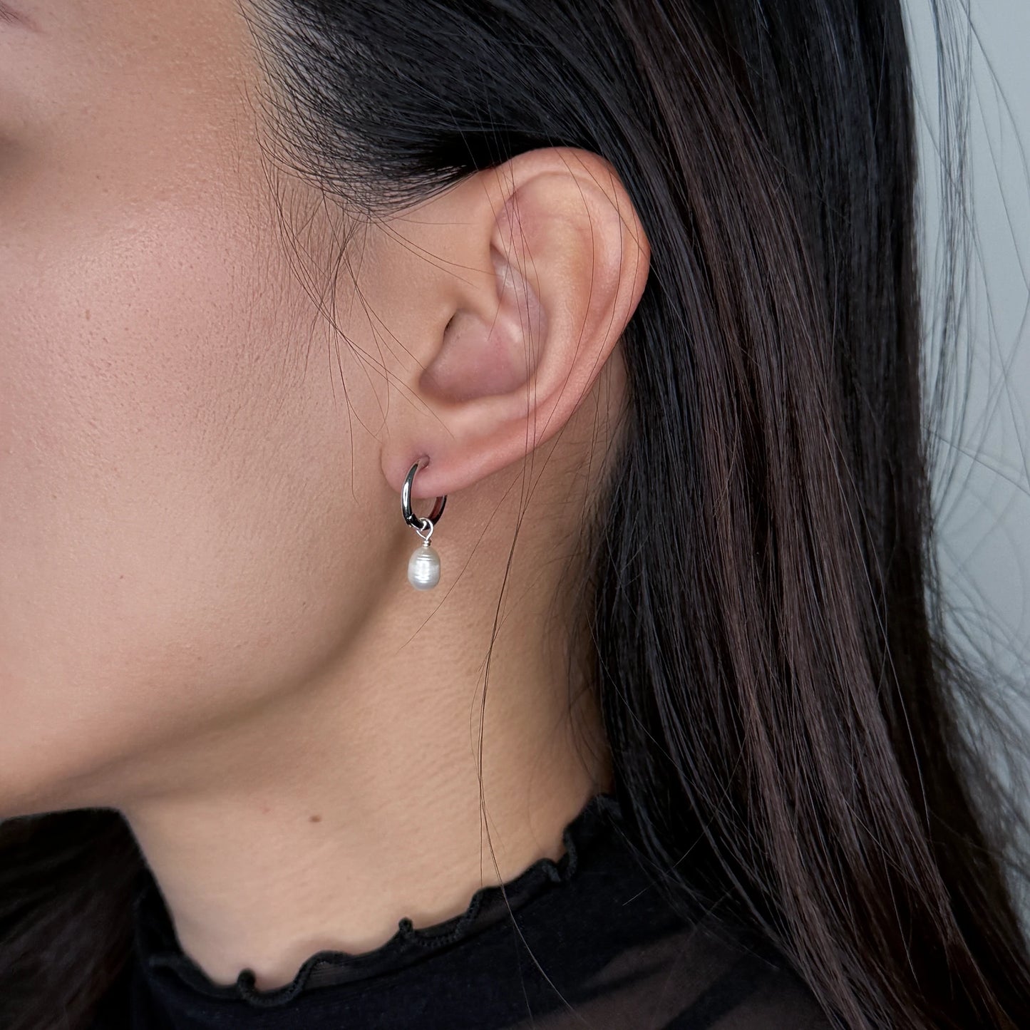 Silver huggies pearl hoop earrings worn by model on a gray background