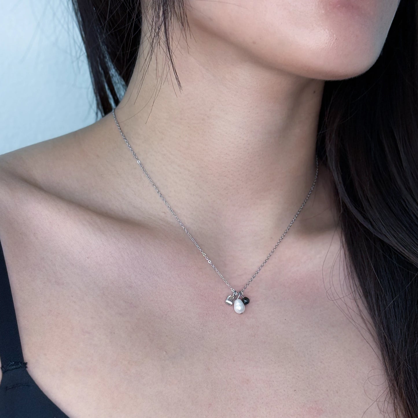 Dainty silver necklace with pearl and glass charms worn on a model