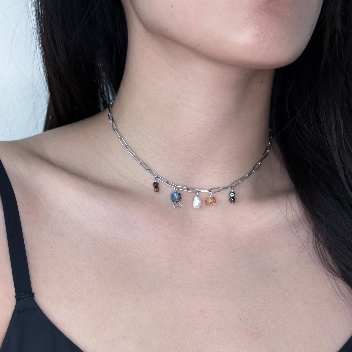 Silver paperclip chain necklace with glass and pearl charms worn by a model