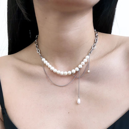 A close-up of a model wearing a multi-layered silver necklace featuring a curved row of white freshwater pearls and two delicate silver chains with a teardrop pearl dangle.