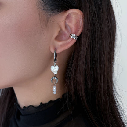 Close-up of an ear wearing a heart-shaped earring with a moon and pearl design.