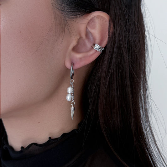 Close-up of an ear wearing a silver earring with pearl drops and a spike, against a neutral background.