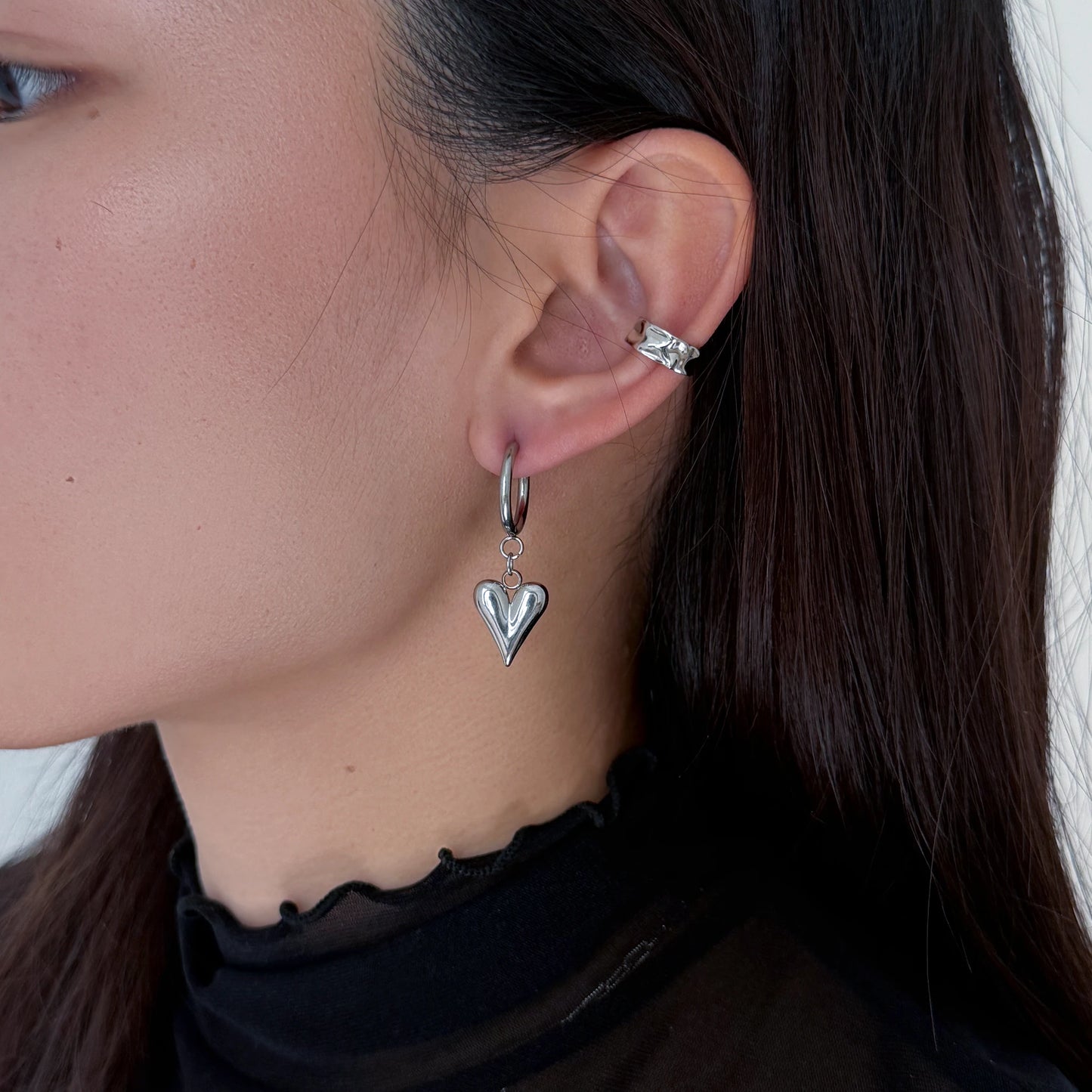 Close-up of a person wearing silver hoop earrings with heart charms.