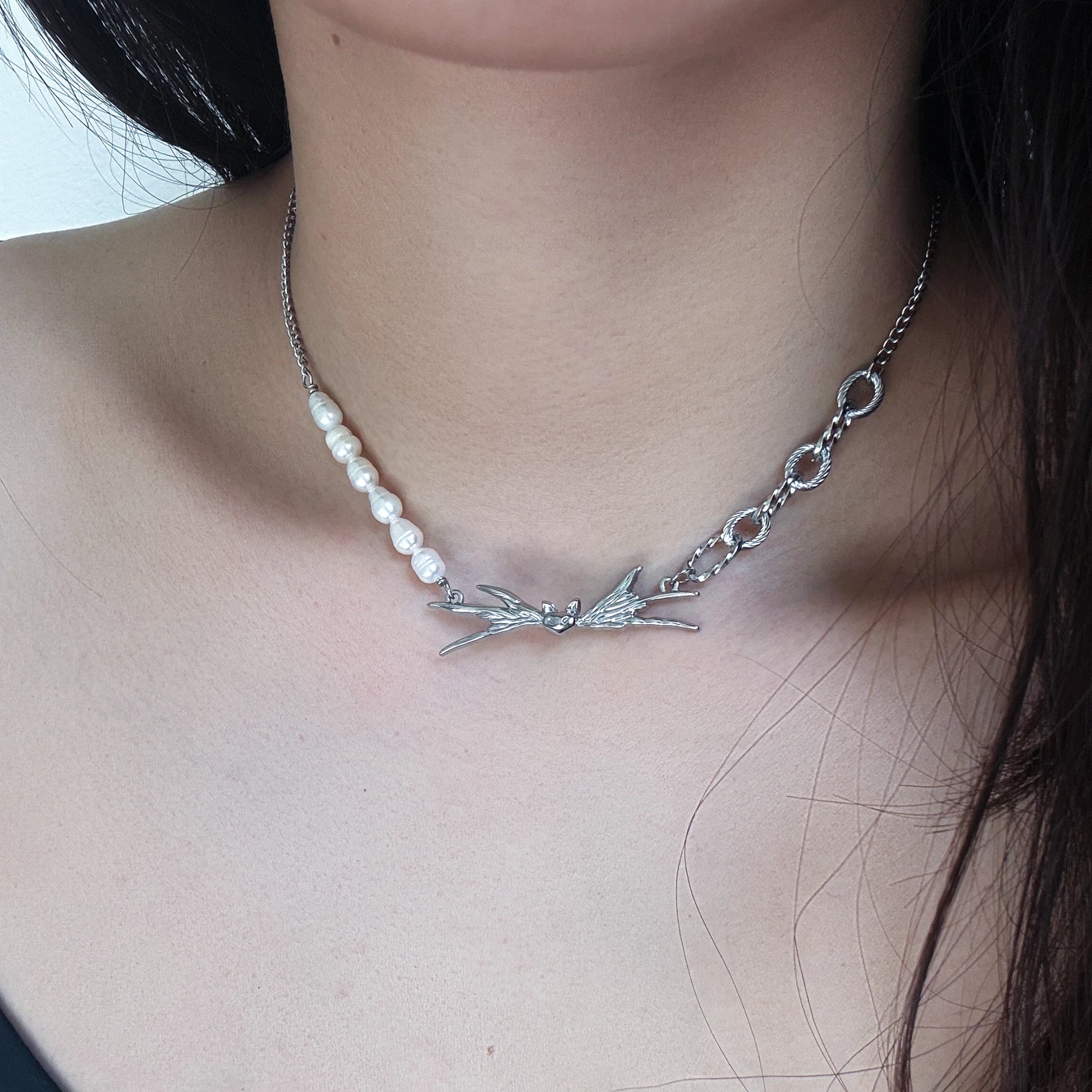 Necklace with pearls and silver winged design on a person's neck