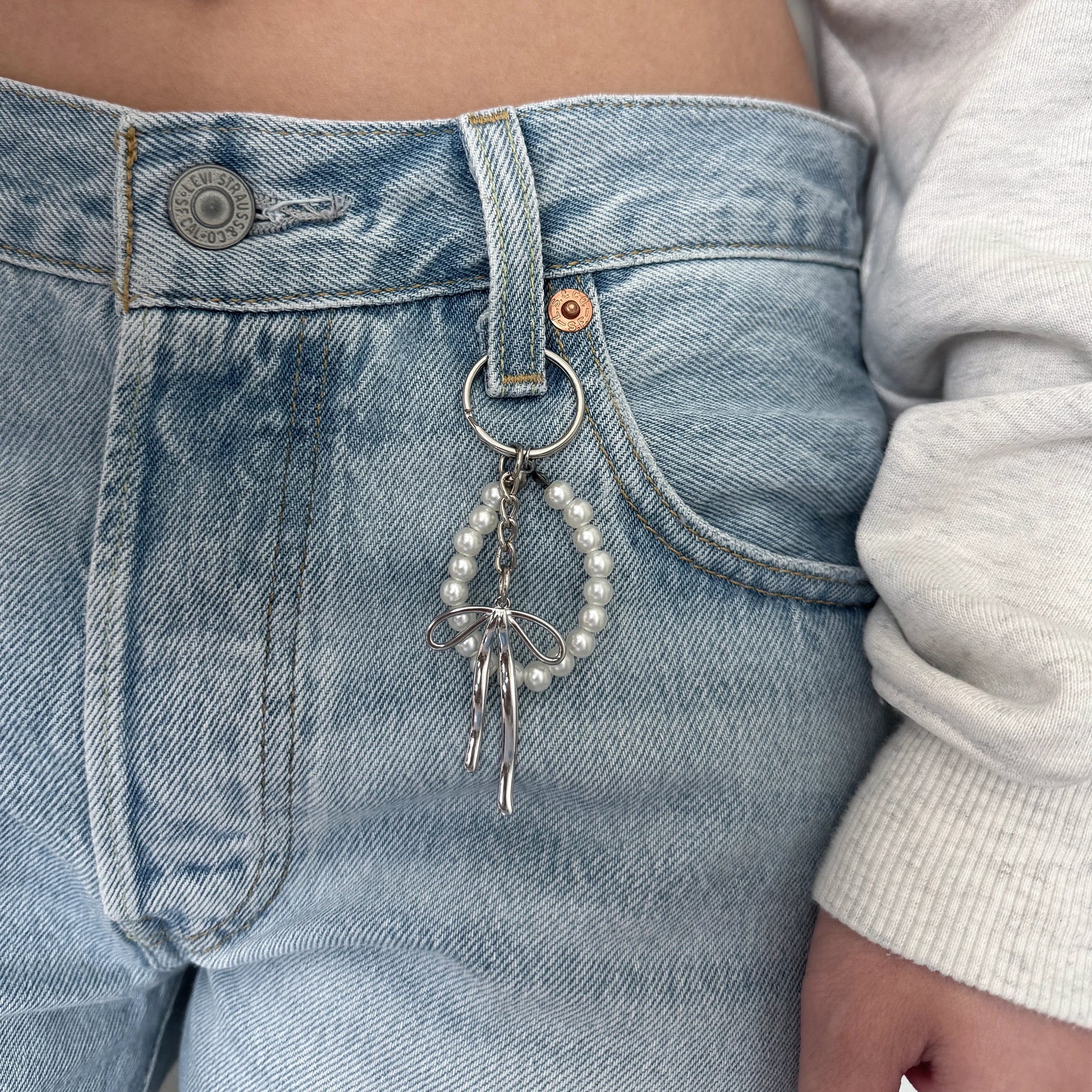 Pearl keychain with silver ribbon on denim jeans