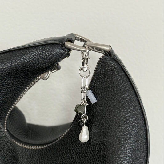 Black leather handbag with a decorative charm featuring beads and a teardrop pendant on a light gray background.