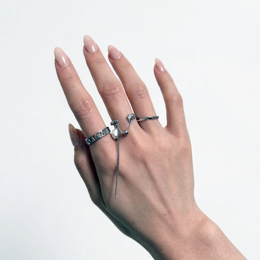 Hand wearing multiple silver rings on a light gray background