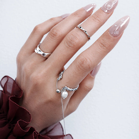 Hand wearing multiple silver rings with a plain background